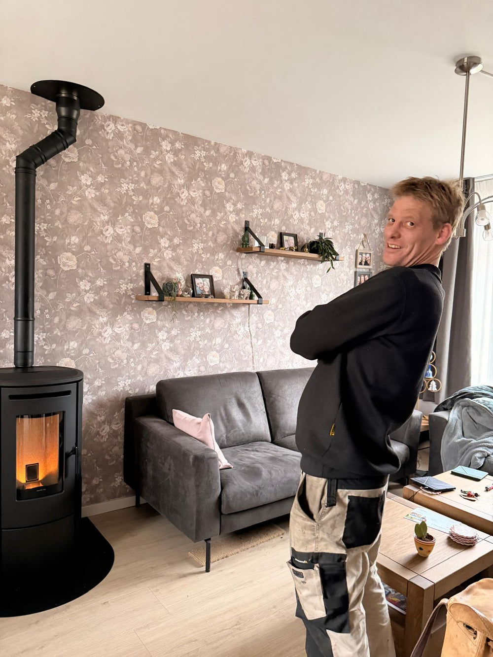 Man standing in a living room with a fireplace and gray sofa.