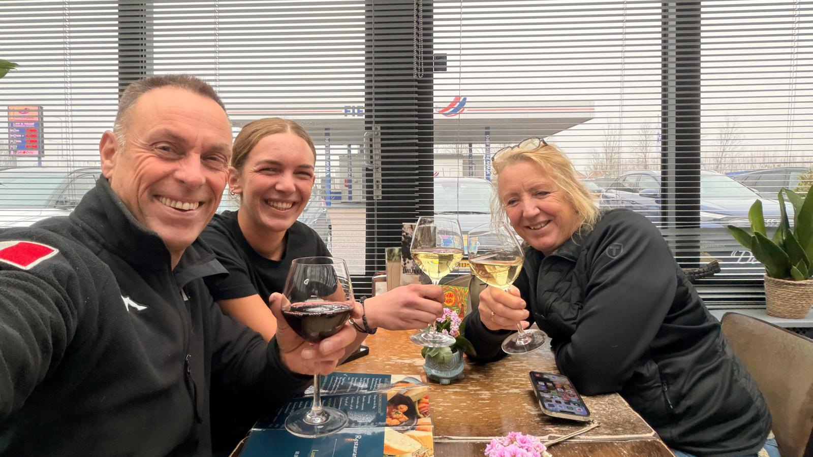 Three people at a table with drinks, smiling and posing for a photo.